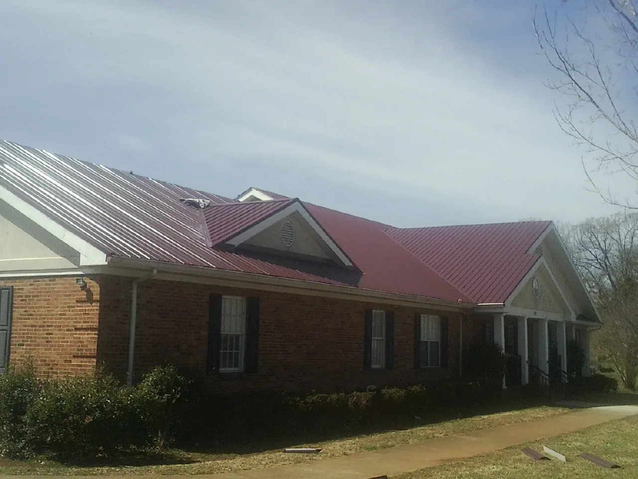 Red metal roof with gabled entries on a long brick building, from a Hail Damage Roof Repair job in Youngstown