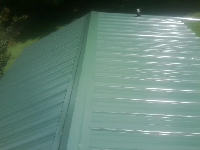 New green metal panels meeting at the ridge of a roof — Flat Roof Repair work by our crew in Youngstown