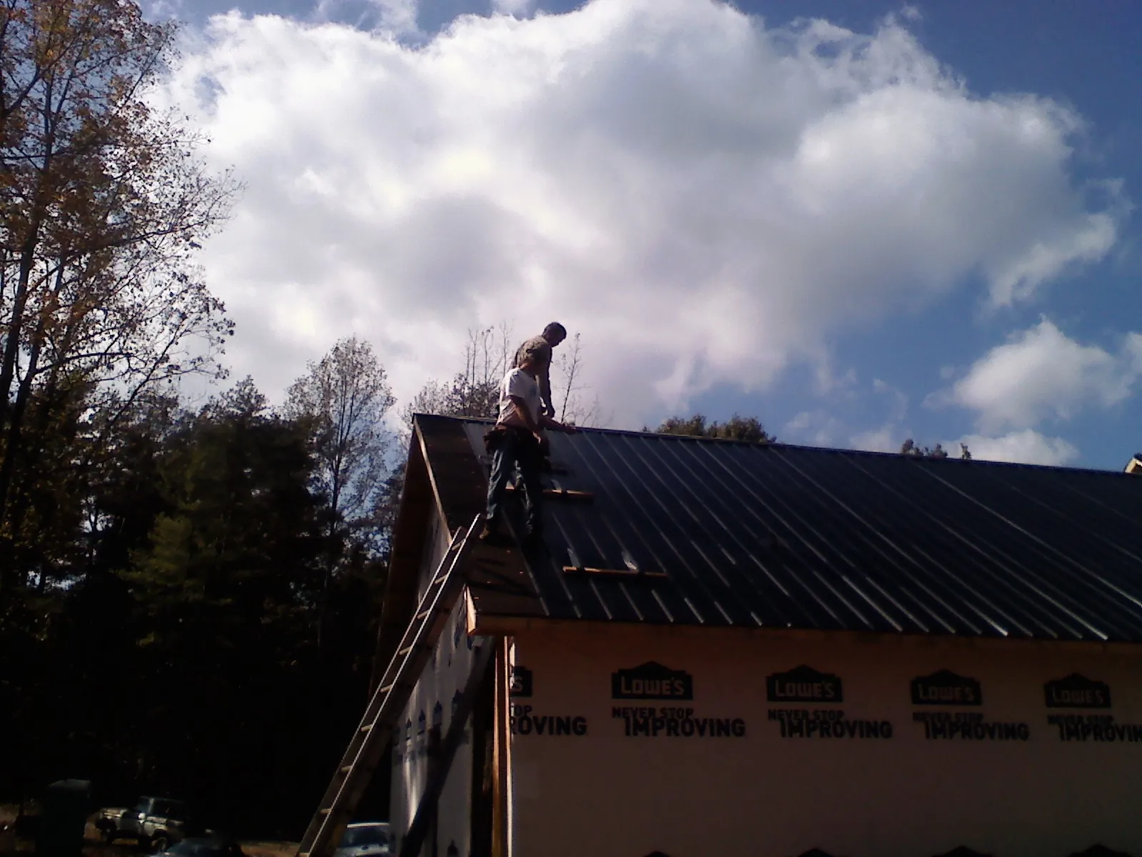 Roofer fastening dark metal panels high against a cloudy sky, from a Roof Inspection job in Youngstown
